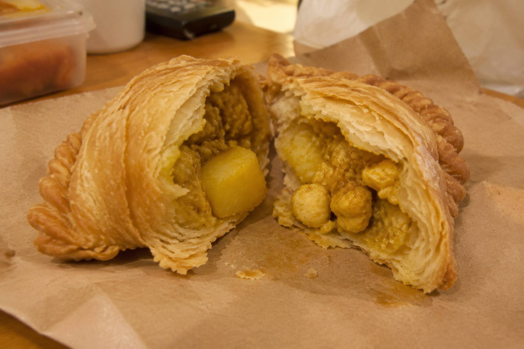 A puff pastry curry puff broken in half on brown paper, showing a yellow curried potato filling