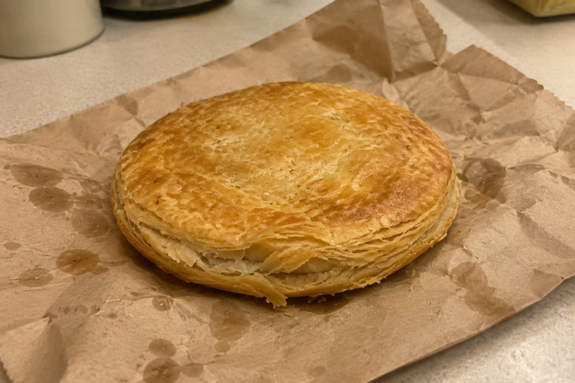 A flat, round, golden all-butter puff pastry chicken pie on a crumpled brown paper bag