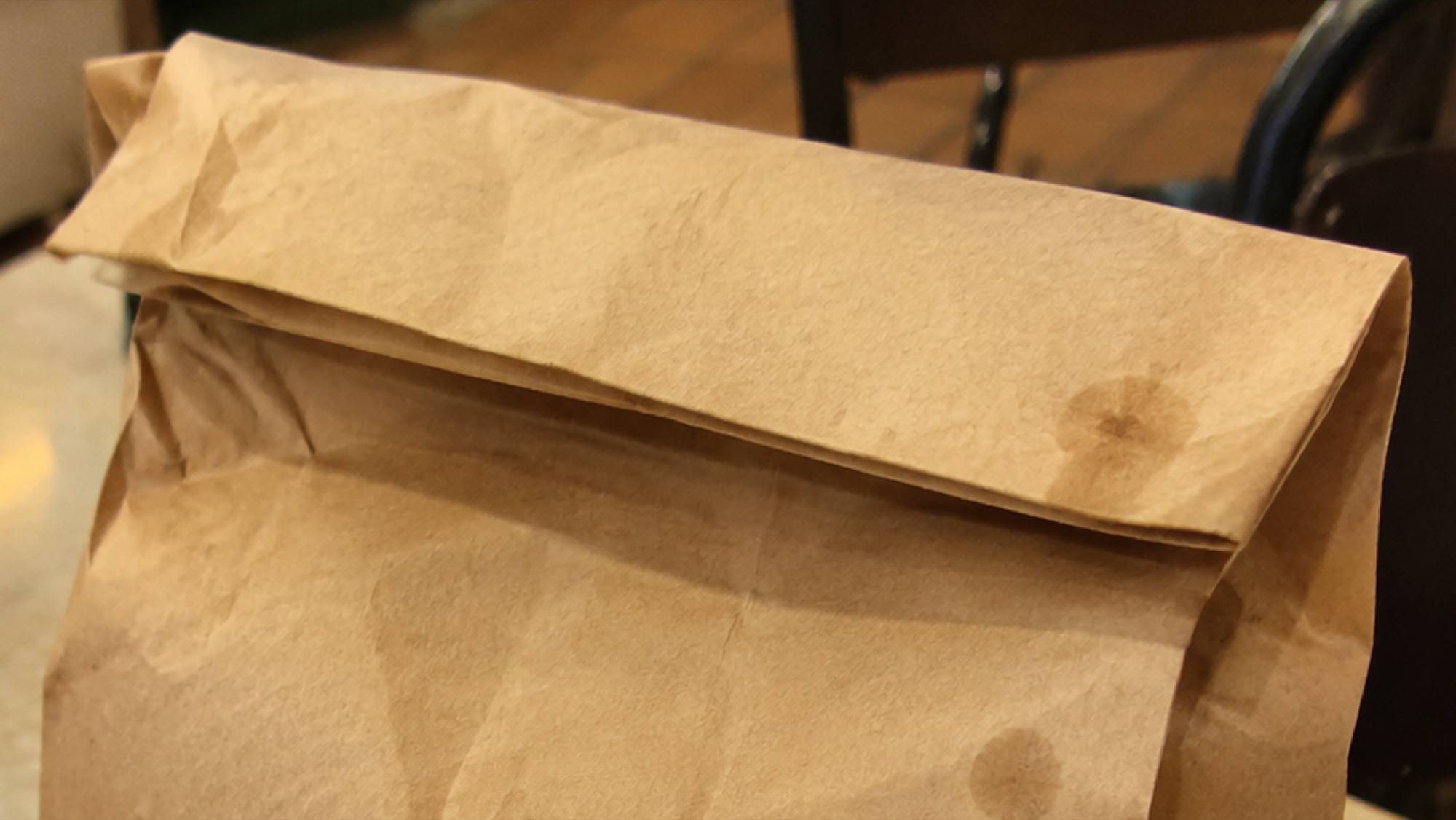 The folded top of a brown paper bag with a grease spot soaking through
