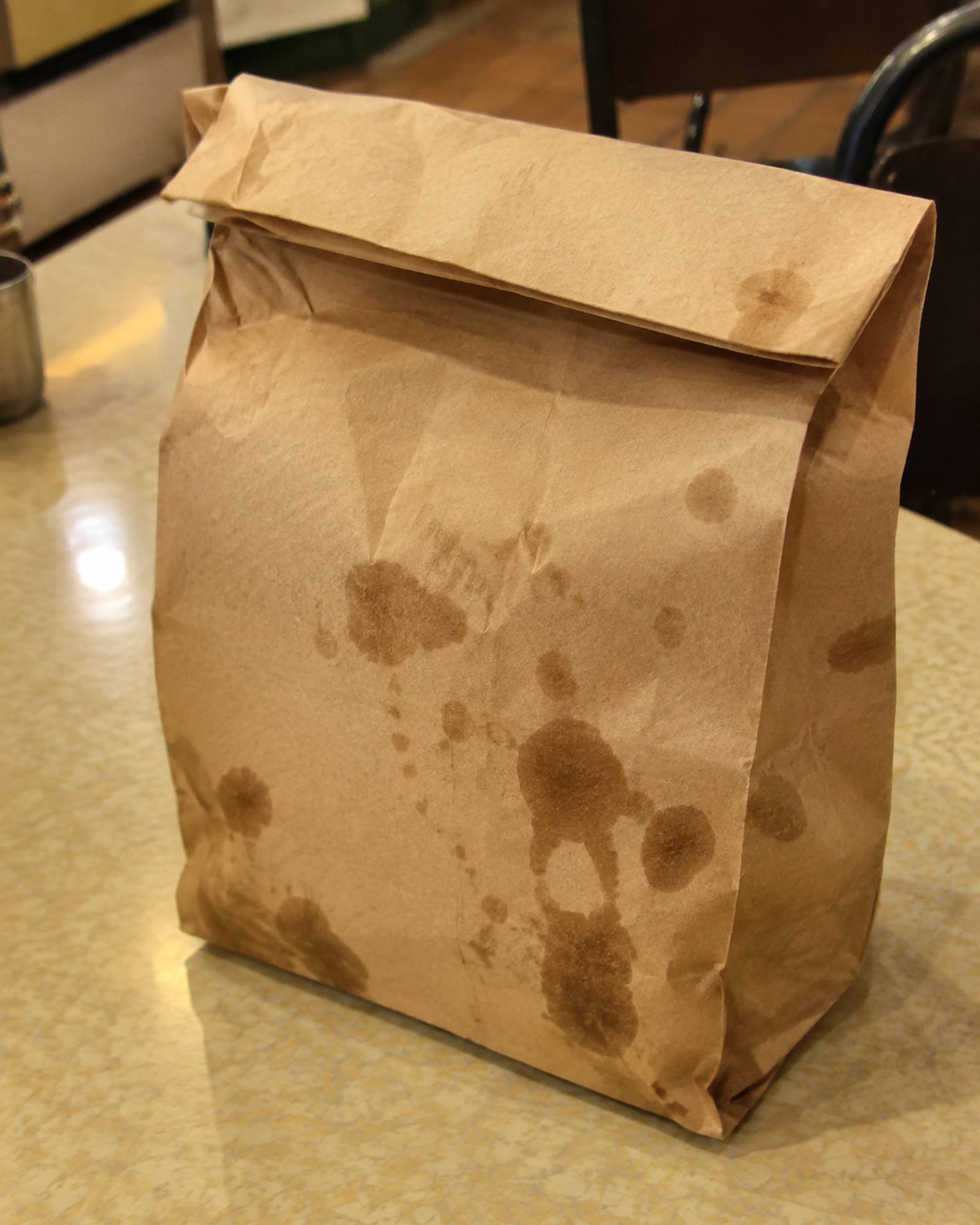 A brown paper bag, top folded over, with grease spots soaking through