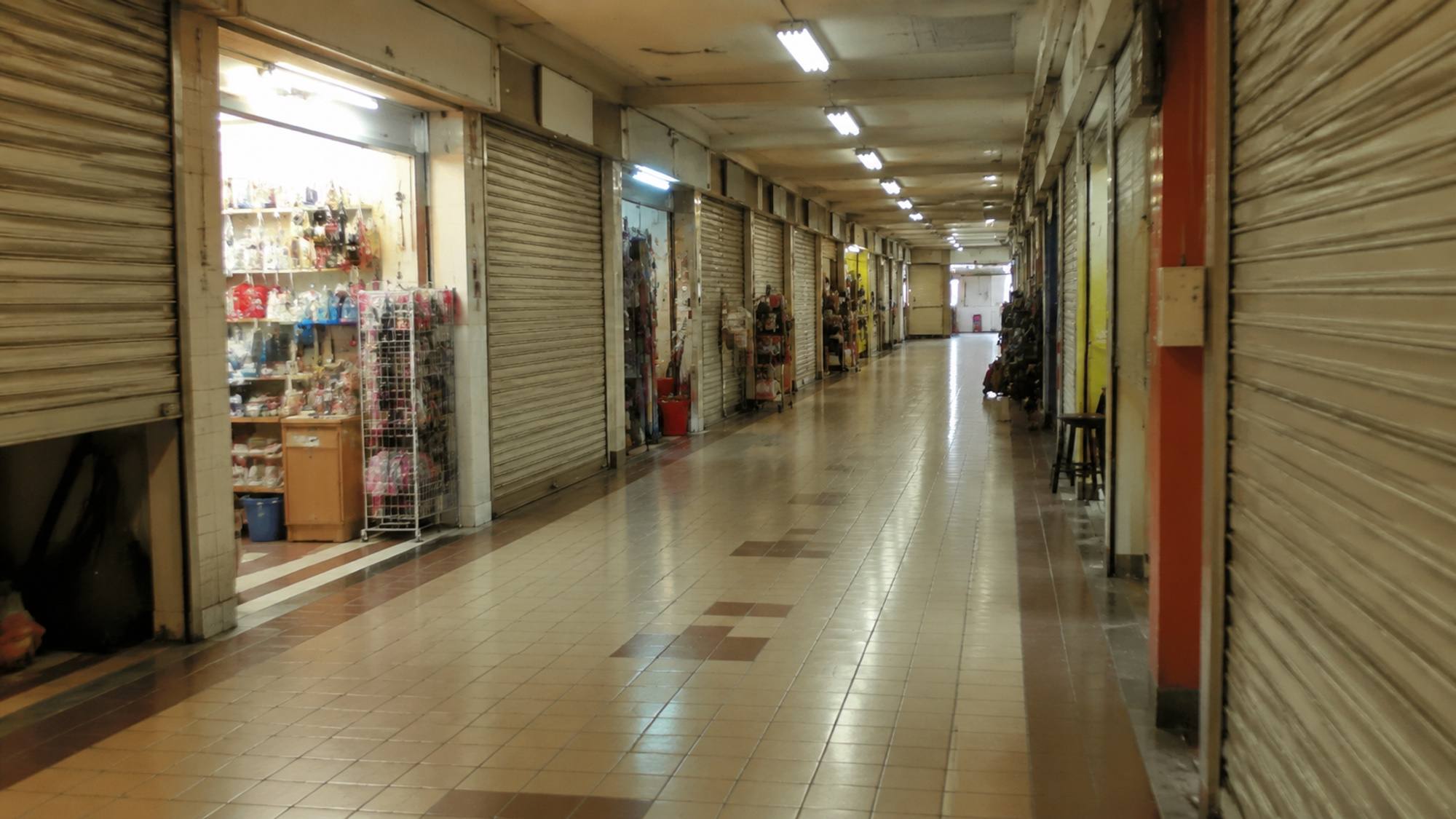 A quiet ground-floor corridor of small shop units with roller shutters